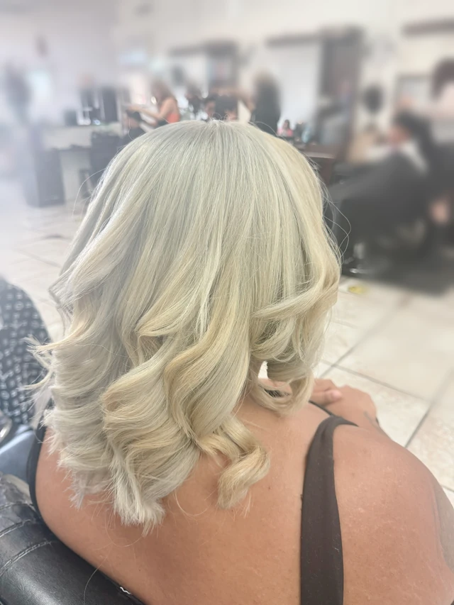 Shoulder-length blonde layered curls with lighter highlights, viewed from behind at an angle.